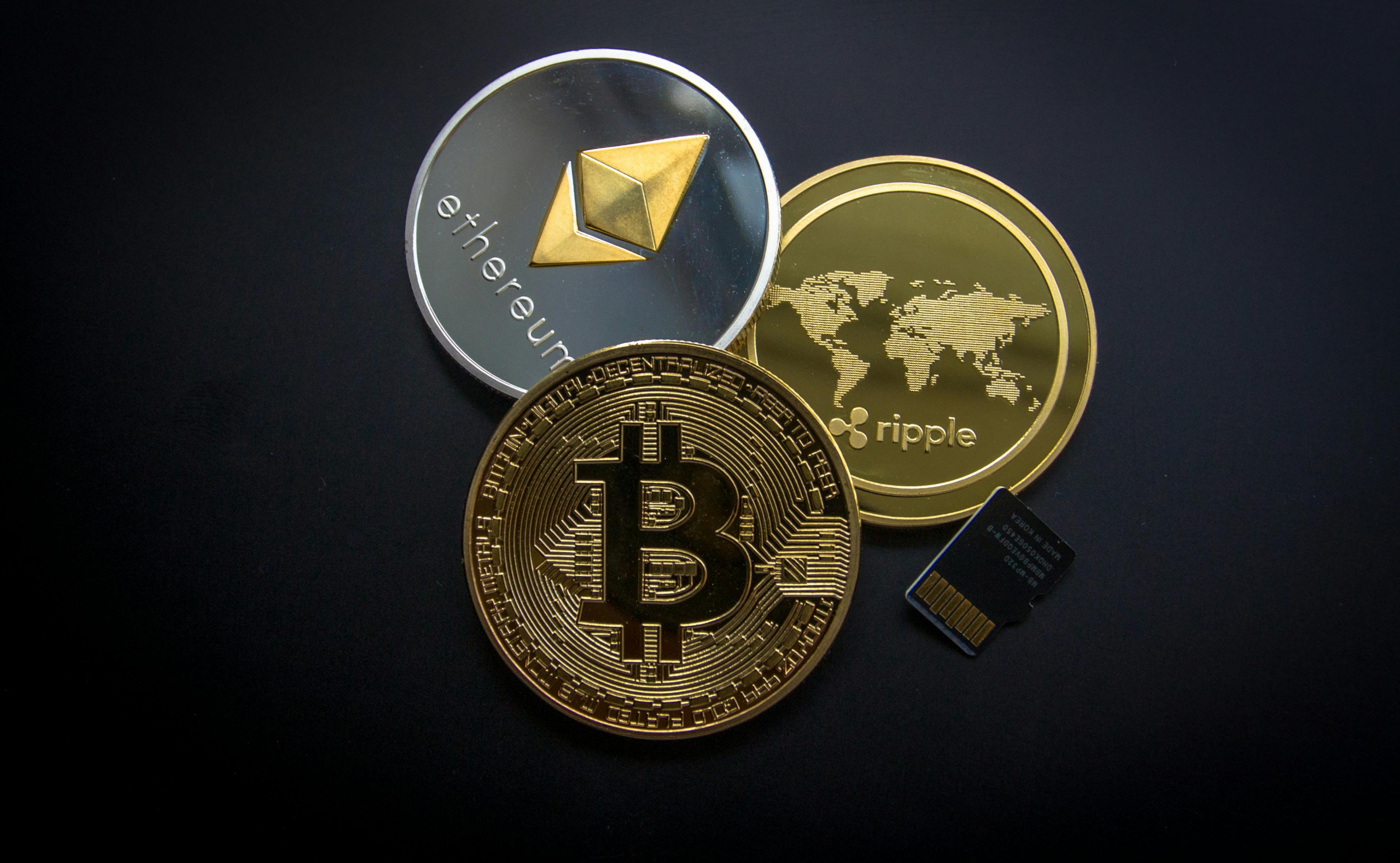 Close-up of physical coins representing Bitcoin, Ethereum, and Ripple on a dark background with a microSD card beside them.